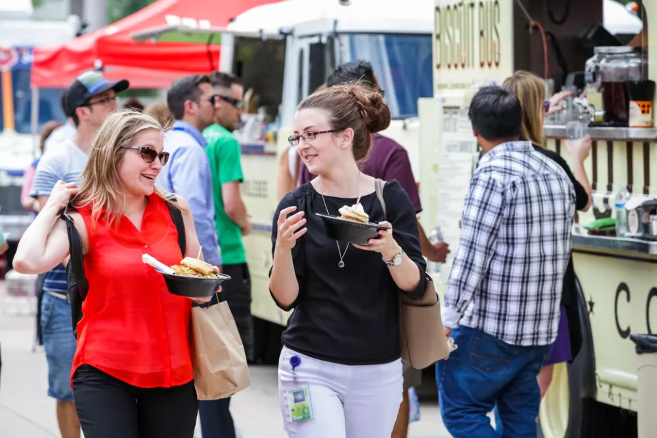 Food truck customers holding food with food trucks in background